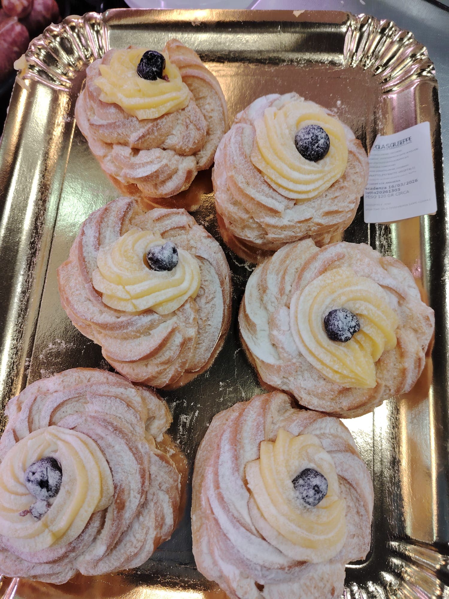 Sei zeppole di San Giuseppe con crema pasticcera e amarena disposte su un vassoio dorato.