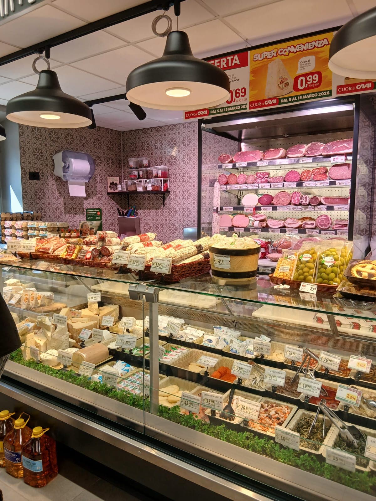 Bancone gastronomia con ampia selezione di formaggi, salumi, olive e piatti pronti in un supermercato.