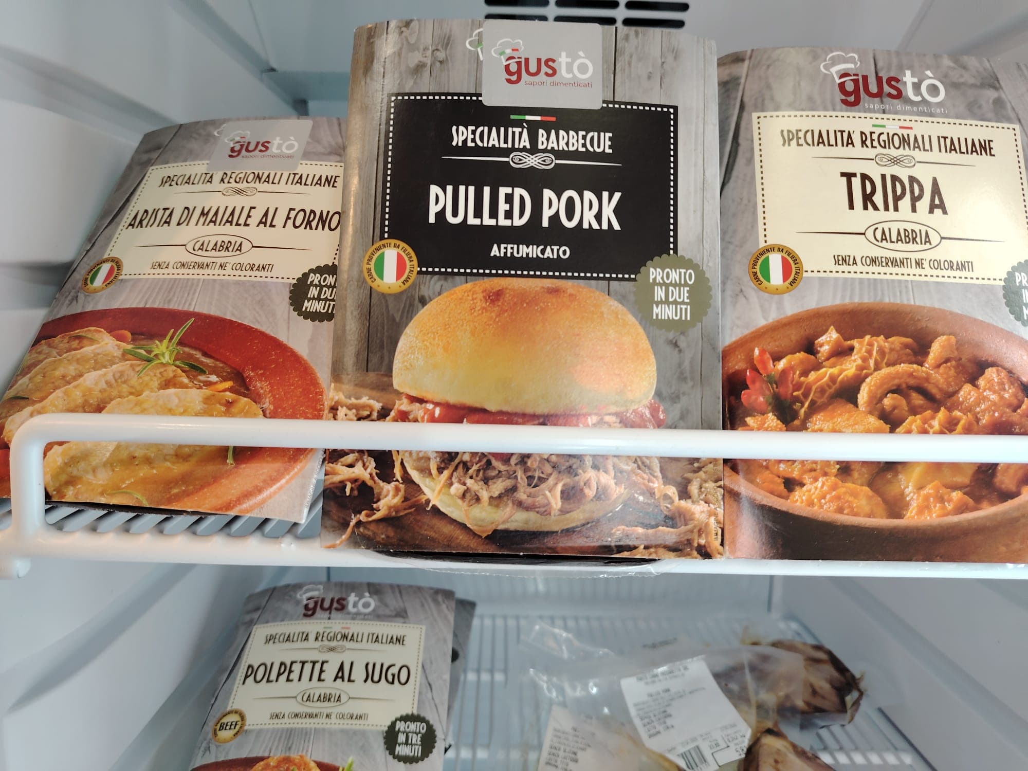Confezioni di piatti pronti Gustò, inclusi pulled pork e trippa, su ripiani di frigorifero.