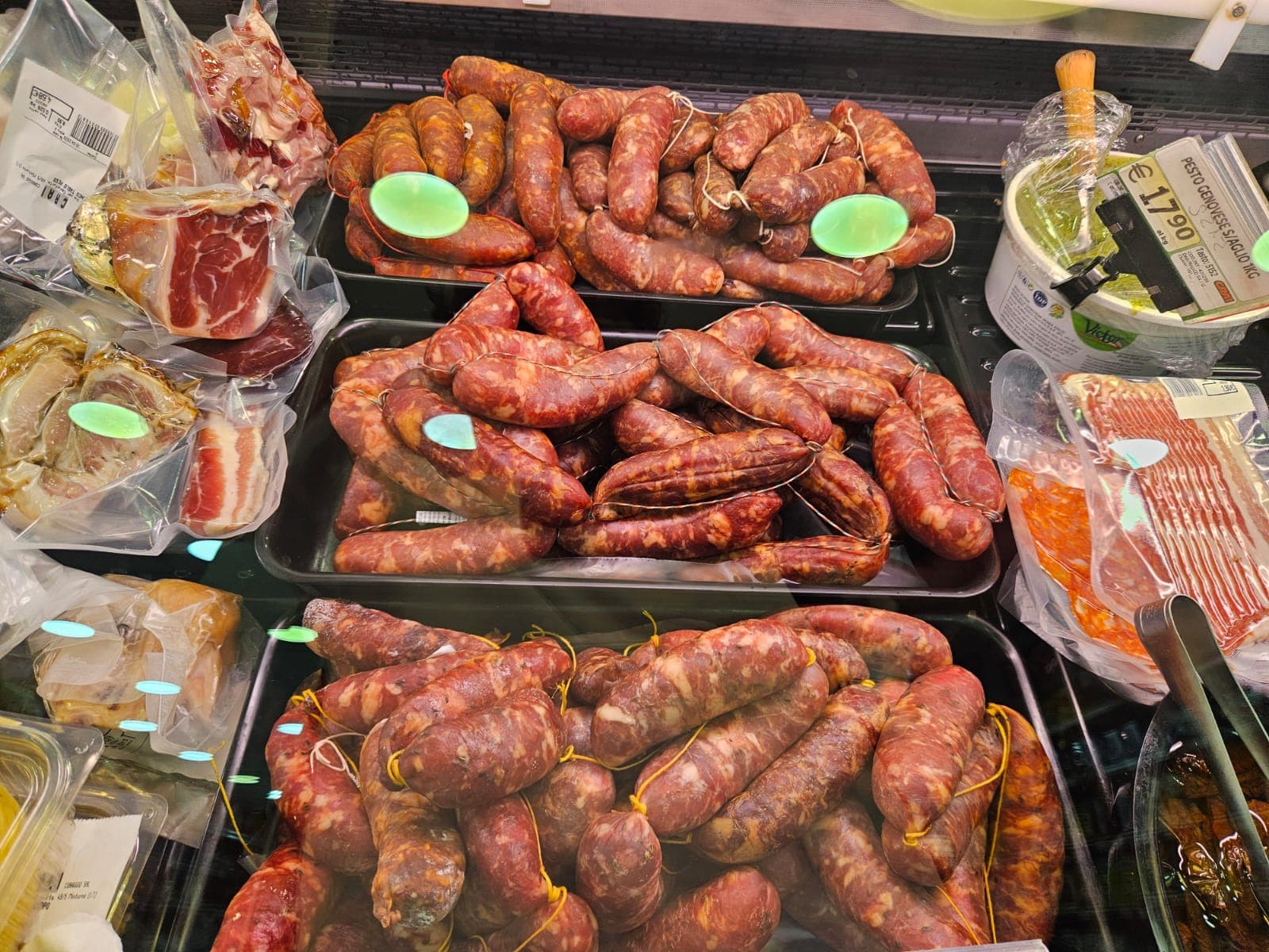 Salsicce fresche e salumi sottovuoto esposti in un banco frigo di una gastronomia.