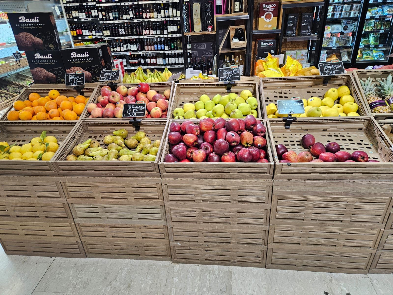 Reparto ortofrutta con cassette in legno contenenti limoni, arance, pere e diverse varietà di mele.