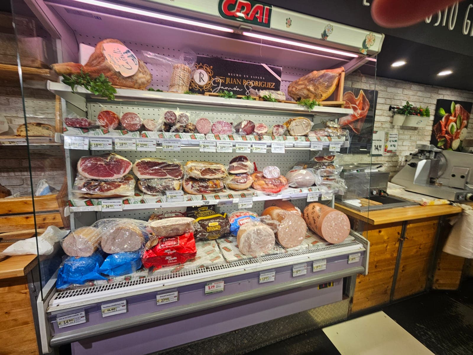 Banco frigo di una salumeria con prosciutti, salami e mortadella esposti su vari ripiani.