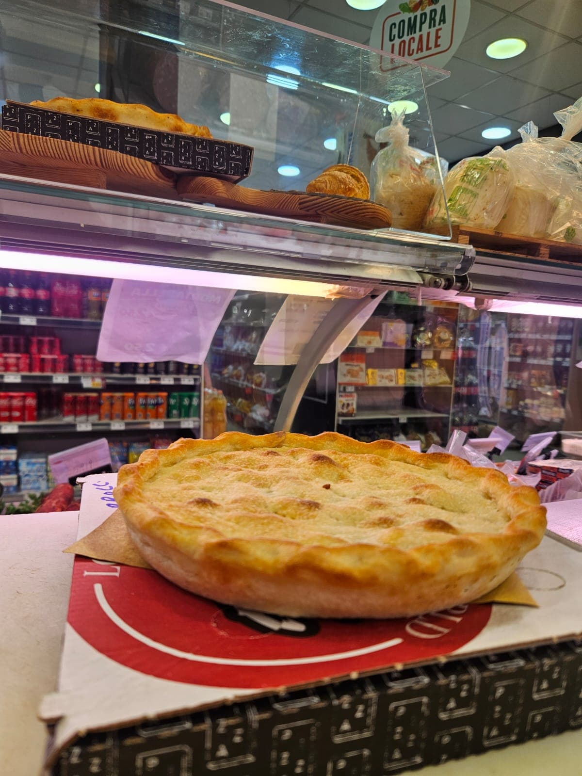 Una grande focaccia dorata con bordi ondulati su un bancone di una gastronomia locale.