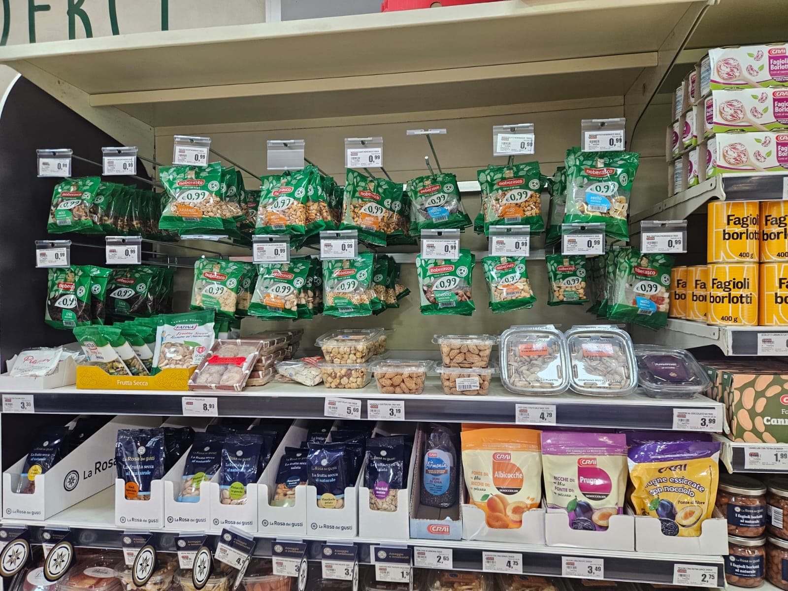 Scaffale di supermercato con assortimento di frutta secca e noci in sacchetti e vaschette.