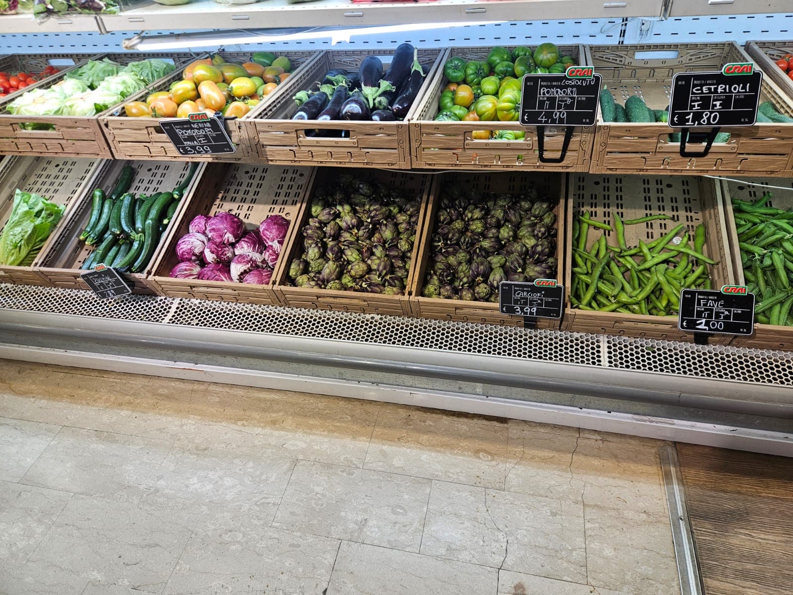 Scaffali di un supermercato con cassette di pomodori, melanzane, zucchine, radicchio, carciofi e fave.