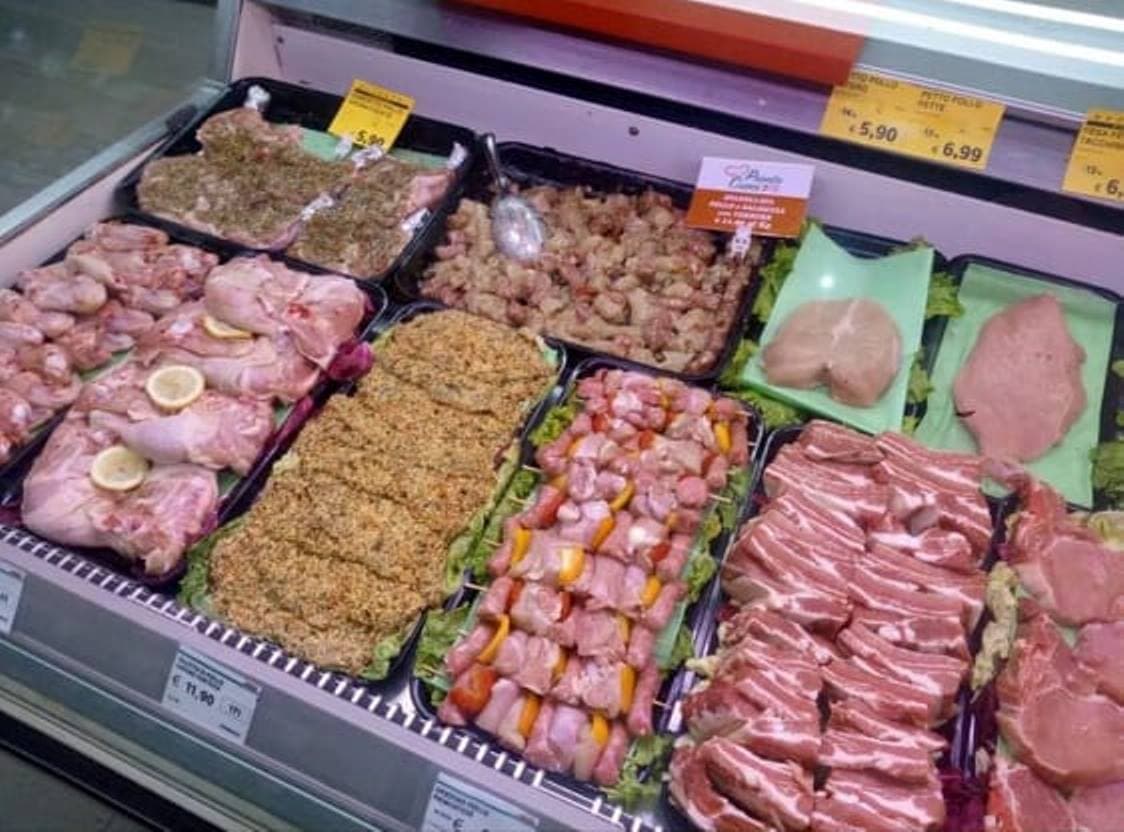 Varietà di tagli di carne cruda, spiedini e preparati pronti da cuocere in un bancone.